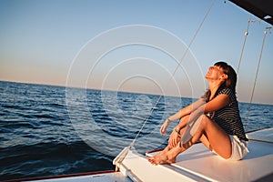 Young pretty smiling woman in striped shirt and white shorts at luxury yacht in sea, sunset