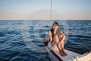 Young pretty smiling woman in striped shirt and white shorts at luxury yacht in sea, sunset