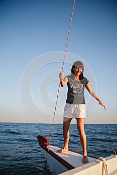 Young pretty smiling woman in striped shirt and white shorts at luxury yacht in sea, sunset