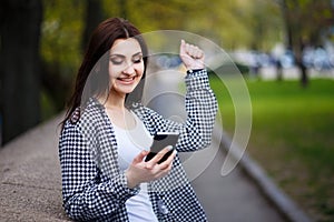Young pretty stylish exulting woman holding smart phone in the s