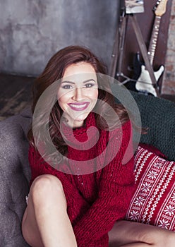 Young pretty stylish woman in red winter sweater at couch in home interior happy smiling, lifestyle people concept