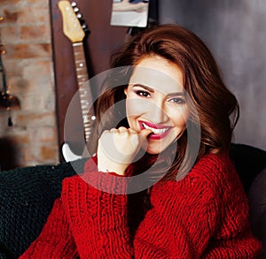 Young pretty stylish woman in red winter sweater at couch in home interior happy smiling, lifestyle people concept