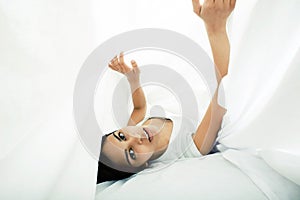 Young pretty tann woman in bed among white sheets having fun, trying to sleep, fooling around