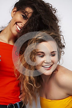 Young pretty teenage girls friends with blond and brunette curly hairs posing cheerful isolated on white background