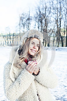 Young pretty teenage hipster girl outdoor in winter snow park having fun drinking coffee, warming up happy smiling