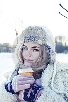 Young pretty teenage hipster girl outdoor in winter snow park having fun drinking coffee, warming up happy smiling