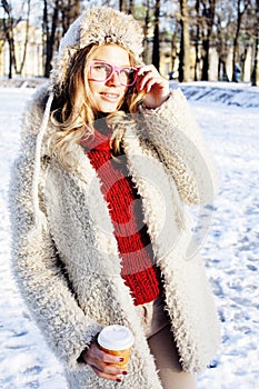 Young pretty teenage hipster girl outdoor in winter snow park having fun drinking coffee, warming up happy smiling