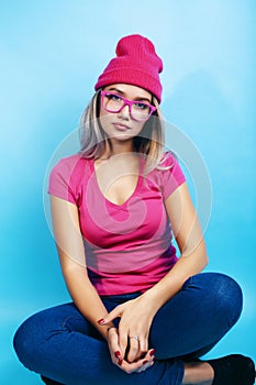 Young pretty teenage modern hipster girl posing emotional happy on blue background, lifestyle people concept