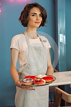 Young pretty waitress in apron serving donuts on a tray