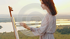 Young pretty woman artist drawing a painting on nature at sunset time