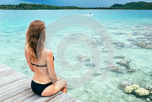 Young pretty woman in black bikini sitting alone on the pier near the sea