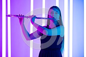 Young pretty woman in black dress plays the flute. Musician female posing in a dark studio against the backdrop of