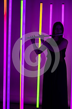 Young pretty woman in black dress plays the flute. Musician female posing in a dark studio against the backdrop of