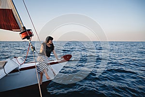 Young pretty woman in black shirt and striped skirt at luxury yacht in sea, sunset