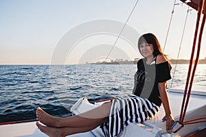 Young pretty woman in black shirt and striped skirt at luxury yacht in sea, sunset