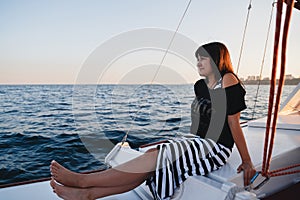 Young pretty woman in black shirt and striped skirt at luxury yacht in sea, sunset