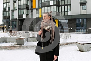 A young pretty woman with blond dreadlocks dressed warmly walks along the street in winter