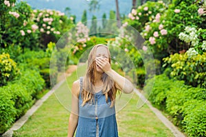 Young pretty woman blowing nose in front of blooming tree. Spring allergy concept