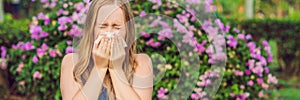 Young pretty woman blowing nose in front of blooming tree. Spring allergy concept BANNER, LONG FORMAT