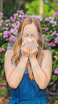 Young pretty woman blowing nose in front of blooming tree. Spring allergy concept VERTICAL FORMAT for Instagram mobile