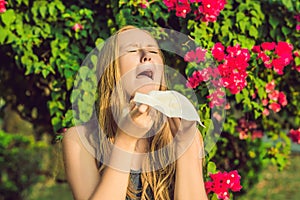 Young pretty woman blowing nose in front of blooming tree. Spring allergy concept