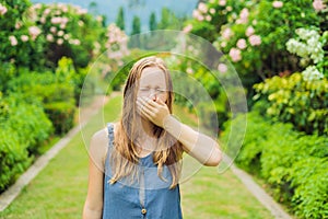 Young pretty woman blowing nose in front of blooming tree. Spring allergy concept