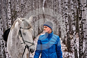 Young pretty woman in a blue jacket and a sports hat for a walk with a white horse