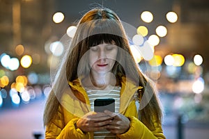 Young pretty woman browsing internet on her mobile phone on a city street at night outdoors