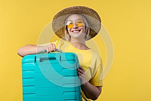 Young pretty woman with carry-on suitcase on yellow background. Teenager traveling with blue luggage bag for airplane