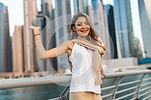Young pretty woman in casual clothes walking on promenade in Dubai with skycrappers on background