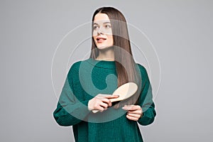 Young pretty woman comb her hairs wearing in green sweater isolated on gray background