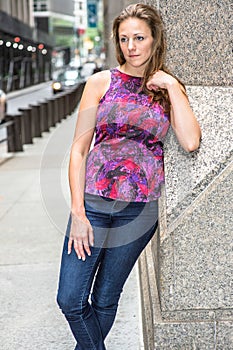 A young pretty woman with damp hair is leaning on a column by the street in New York City, thinking