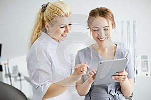 A young pretty woman dentist and her assistant are standing in the middle of the office with a tablet in their hands