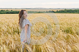Young pretty woman in dress poses on wheat field