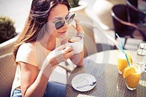 Young pretty woman drinking cappuccino, coffee in cafe outdoors