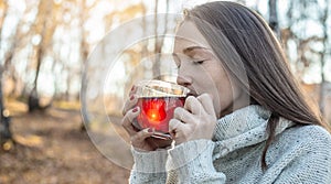 Young woman is drinking hot tea in an autumn Park in the light of the sunset. Cozy lifestyle in the autumn cold season