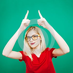 Young Pretty Woman in Eyeglasses and Red Top is Showing Up by Two Fingers. Studio Short of Beautiful Girl on Green