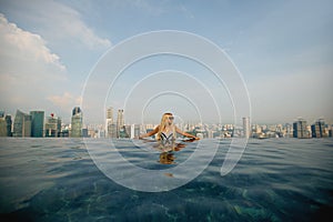 A young pretty woman in a fashionable swimsuit posing on the edge of the infinity pool on the top of the building with a