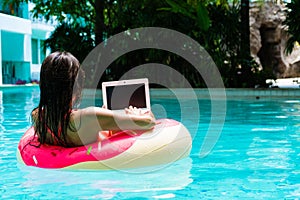 Young pretty woman freelancer is floating on the sea or in the pool in a swimming circle. A girl is relaxing on the