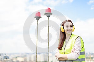 Young pretty woman in green west and earmuffs stand on roof, hold tablet