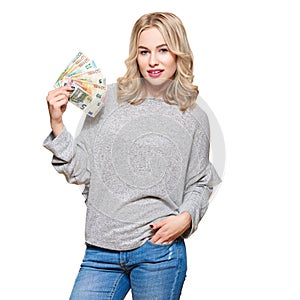 Young pretty woman in grey sweater holding bunch of Euro banknotes, looking at camera and smiling, isolated on white background.