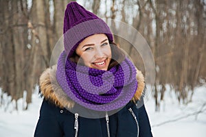 Young pretty woman with happy smile in purple snood and hand-knitted hat.