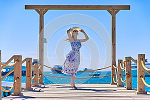 Young pretty woman in a hat standing alone on the pier near the sea and looking on the water and waiting for somebody in ocean