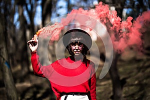 Young pretty woman holding red colorful smoke bomb on the outdoor park. Red smoke spreading in the cerebration festival