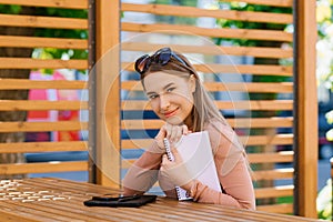 Young pretty woman holds a notebook in her hands and sits at a table in a street cafe or a cavorting photo