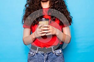 Young pretty woman holds takeout coffee stands over blue wall