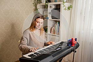 Young pretty woman at home playing on synthesizer for followers