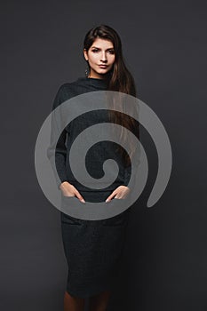 Young pretty woman in knitted dress posing over dark grey background