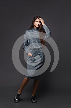 Young pretty woman in knitted dress posing over dark grey background
