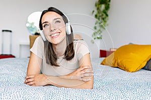 Young pretty woman listening music with wireless headphones while lying on bed